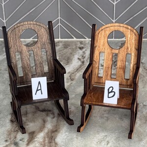 Peut inclure: Deux petites chaises &agrave; bascule en bois, une marron fonc&eacute; et une marron clair, sont pr&eacute;sent&eacute;es c&ocirc;te &agrave; c&ocirc;te. Chaque chaise a un dossier arrondi avec une d&eacute;coupe circulaire et des lattes verticales. De petites cartes blanches &eacute;tiquet&eacute;es "A" et "B" sont plac&eacute;es sur les si&egrave;ges.