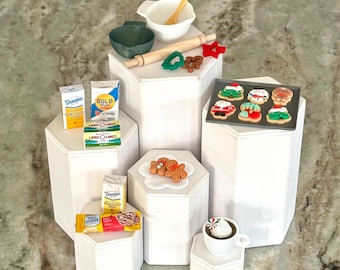 May include: Miniature Christmas baking scene with a variety of items. Includes a mixing bowl, rolling pin, cookie cutters, and a baking sheet of decorated cookies. Also features miniature packages of sugar, butter, and chocolate chips, plus a cup of hot cocoa.