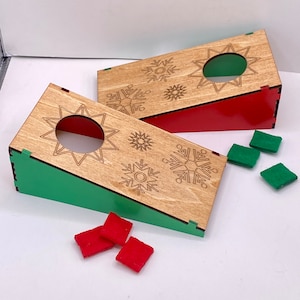 May include: Two wooden game boards with a green and red painted base. Each board has a star-shaped hole and snowflake designs. The boards are accompanied by red and green felt squares.