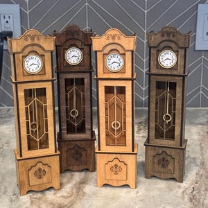 May include: Four miniature grandfather clocks made of wood in varying shades of brown. Each clock features a white circular face with black numerals, a glass-fronted middle section with a visible pendulum, and a decorative fleur-de-lis on the base.