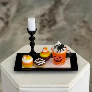 May include: A miniature black rectangular tray holding a black candlestick with a white candle, a candy corn cupcake, a chocolate donut with white icing, and an orange mug with a jack-o'-lantern face, white whipped topping, and a black spider.