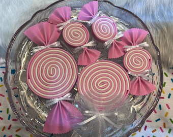 May include: Pink and white candy cane shaped ornaments with a white tulle bow. The ornaments are arranged in a glass bowl.