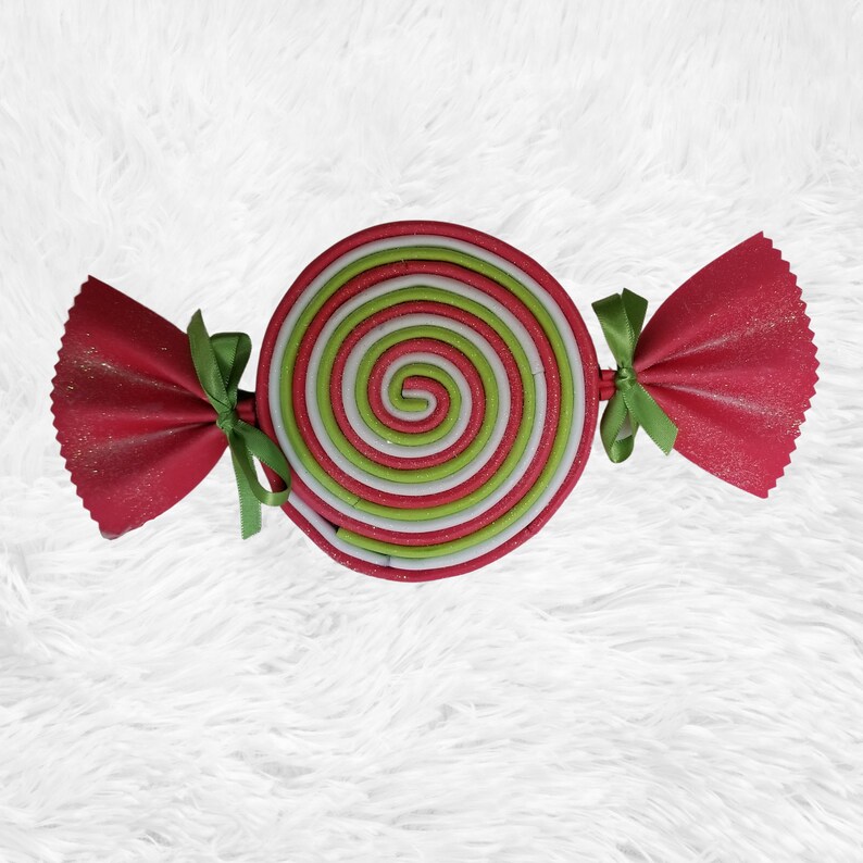 May include: A red and green candy cane shaped ornament with a white swirl design. The ornament is made of fabric and has a red and green ribbon.