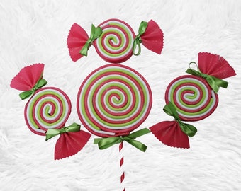 May include: A set of five red and green candy lollipops with white stripes. The lollipops are decorated with pink bows and green ribbon.