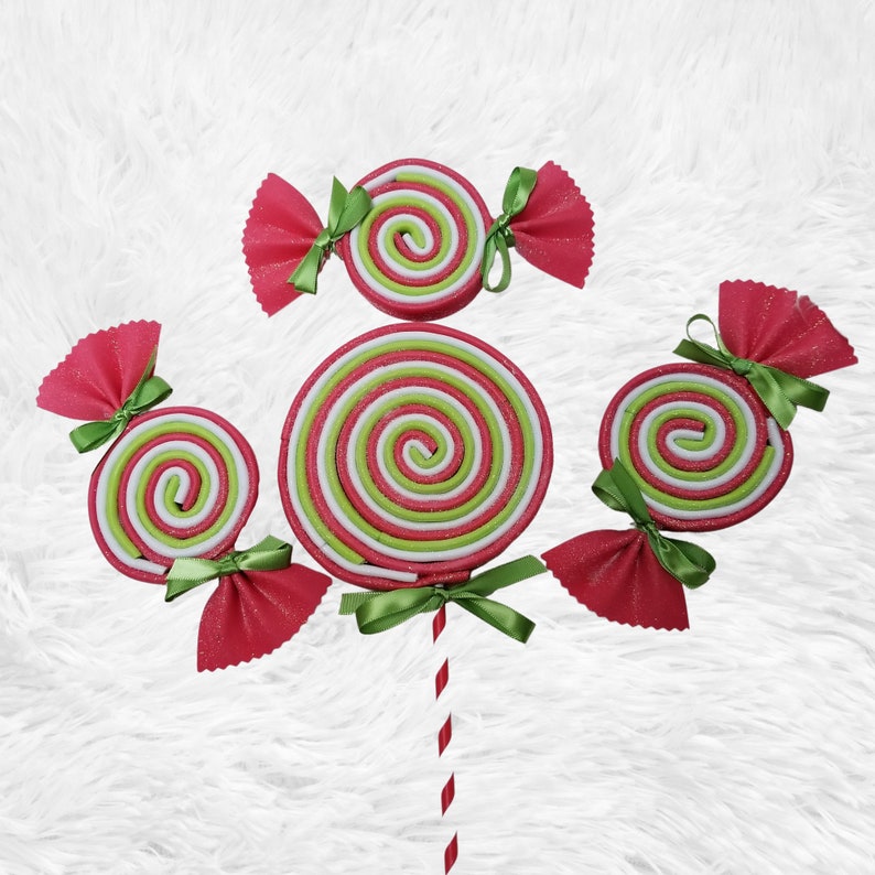 May include: A set of five red and green candy lollipops with white stripes. The lollipops are decorated with pink bows and green ribbon.