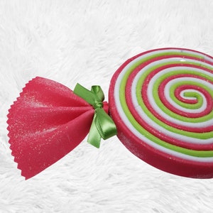 May include: A red and green candy cane ornament with a sparkly finish. The candy cane is made of fabric and has a bow.