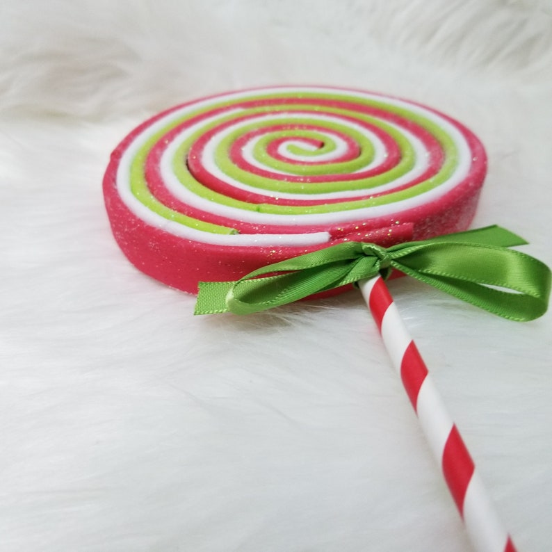 May include: A large, pink, green, and white swirl lollipop with a red and white striped stick. A green ribbon is tied around the stick.