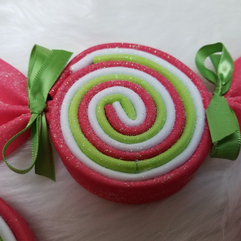 May include: A red, white, and green candy cane ornament with glitter. The candy cane is tied with a green ribbon.
