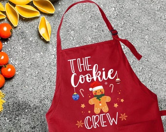 Könnte beinhalten: Rote Weihnachts-Schürze mit einem weißen Lebkuchenmann-Motiv und dem Text "The Cookie Crew".