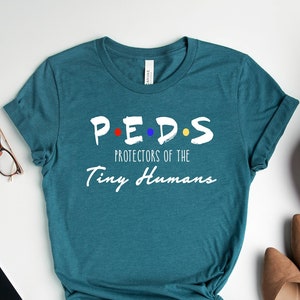 May include: Teal blue t-shirt with white text that reads "P.E.D.S. Protectors of the Tiny Humans". The letters in "PEDS" are decorated with small colored dots.
