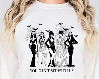 May include: White sweatshirt with a black and white illustration of four women with long hair and black dresses. The women are standing in a row and have a spiderweb and bats behind them. The text "YOU CAN'T SIT WITH US" is printed below the illustration.