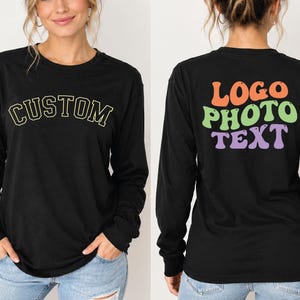 May include: A black long-sleeve shirt featuring the word CUSTOM in a yellow arched font on the front. The back displays the words LOGO PHOTO TEXT in a stacked, wavy, multi-coloured font with orange, light green, and purple lettering.