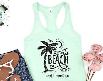 May include: A mint green tank top with a black graphic of a palm tree, sun, and the text "The Beach is Calling and I must go." The tank top is paired with denim shorts and brown sandals. A bouquet of pink flowers is also present.