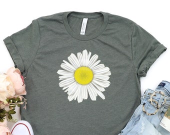 May include: A dark green t-shirt with a white daisy graphic. The daisy has a yellow center and white petals. The t-shirt is shown with a pair of light blue denim shorts and white sneakers.