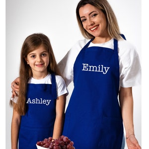 May include: Two blue aprons with white text. The larger apron says "Emily" and the smaller apron says "Ashley".