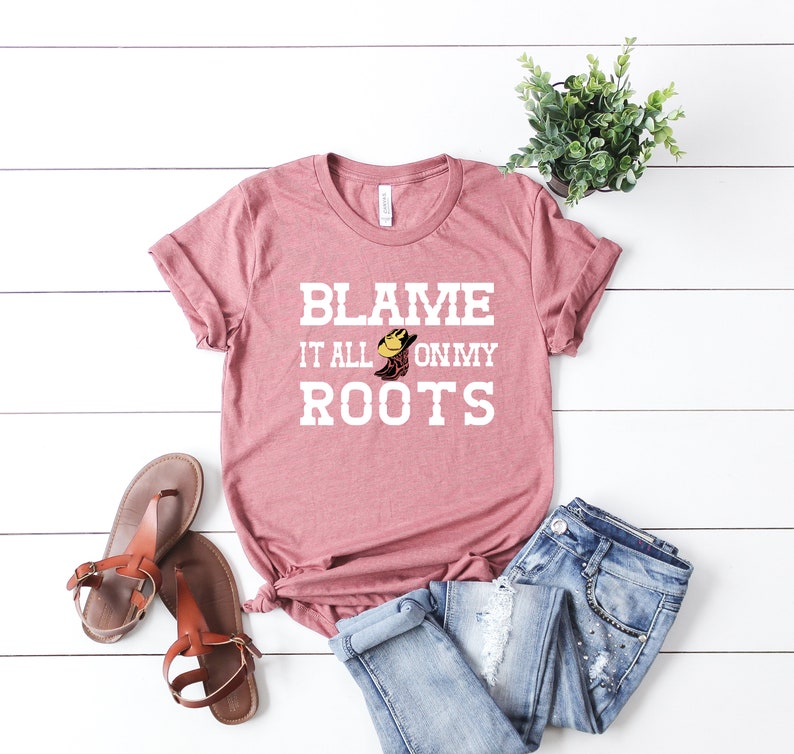 May include: A dusty rose t-shirt with the text "Blame it all on my roots" in white with a cartoon boot graphic.