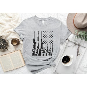 May include: A gray t-shirt with a black and white graphic of guns arranged in the shape of an American flag.