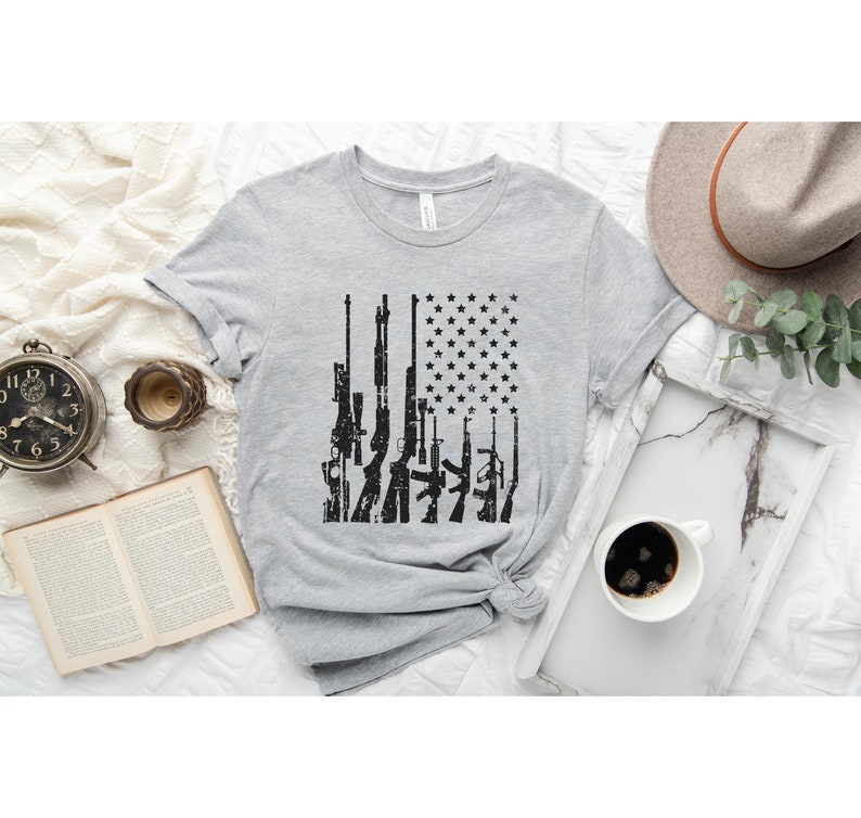 May include: A gray t-shirt with a black and white graphic of guns arranged in the shape of an American flag.