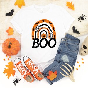 May include: White t-shirt with an orange and black rainbow design featuring a pumpkin and the word "BOO".