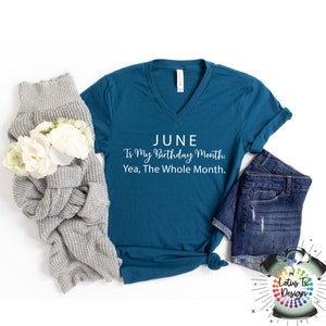 Puede incluir: Camiseta azul turquesa de cuello en V con el texto "JUNE Is My Birthday Month: Yea, The Whole Month." en letras blancas. La camiseta est&aacute; colocada sobre una superficie blanca con un su&eacute;ter gris y unos pantalones cortos de mezclilla azul.