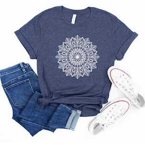 May include: A navy blue t-shirt with a white mandala design. The shirt is shown with blue jeans and white sneakers.