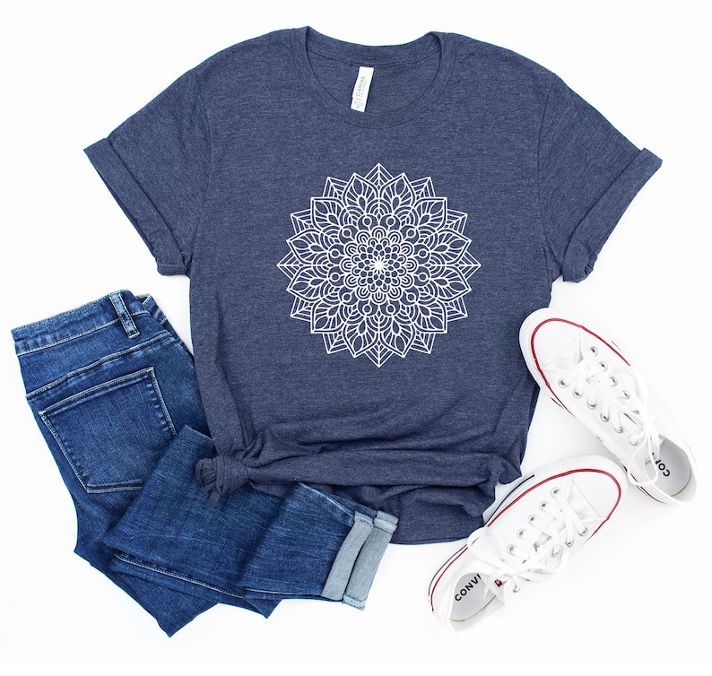 May include: A navy blue t-shirt with a white mandala design. The shirt is shown with blue jeans and white sneakers.