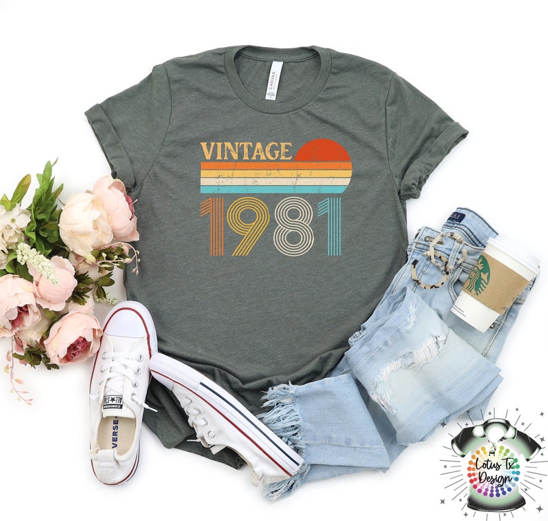May include: A dark green t-shirt with a vintage 1981 design. The design features a sunset with a rainbow stripe and the year 1981 in a retro font.