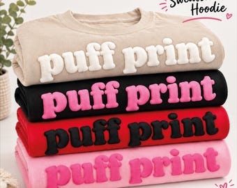 May include: A stack of four sweatshirts with hoodies, each featuring the text "puff print" in a raised, three-dimensional font. The colors from top to bottom are beige with white text, black with pink text, red with black text, and light pink with pink text.
