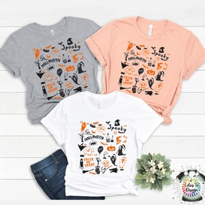 Puede incluir: Tres camisetas con tem&aacute;tica de Halloween. Las camisetas son grises, melocot&oacute;n y blancas. Cada camiseta tiene un dise&ntilde;o en negro y naranja con las palabras "Spooky Halloween" y "Trick or Treat".