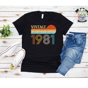 May include: Black t-shirt with a vintage 1981 design featuring a sunset and striped lines in orange, yellow, blue, and white.