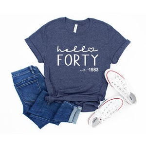 May include: A navy blue t-shirt with the text "hello forty est. 1983" in white. The text includes a small heart symbol.