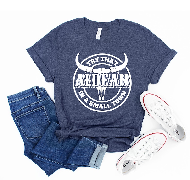 May include: A navy blue t-shirt with a white graphic of a bull skull with the text "Try That In A Small Town" and "ALDEAN" in a circle around the skull.