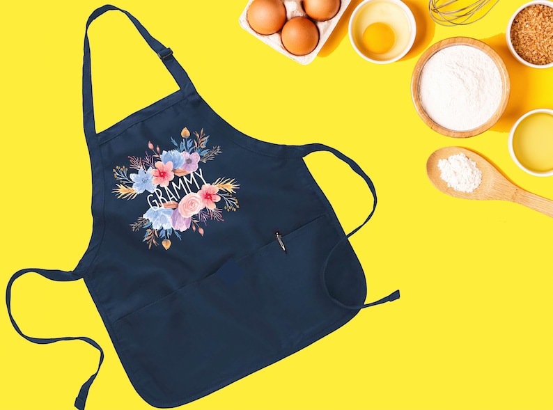May include: Navy blue apron with a floral design and the word "GRAMMY" in white text. The apron has a large pocket on the front.
