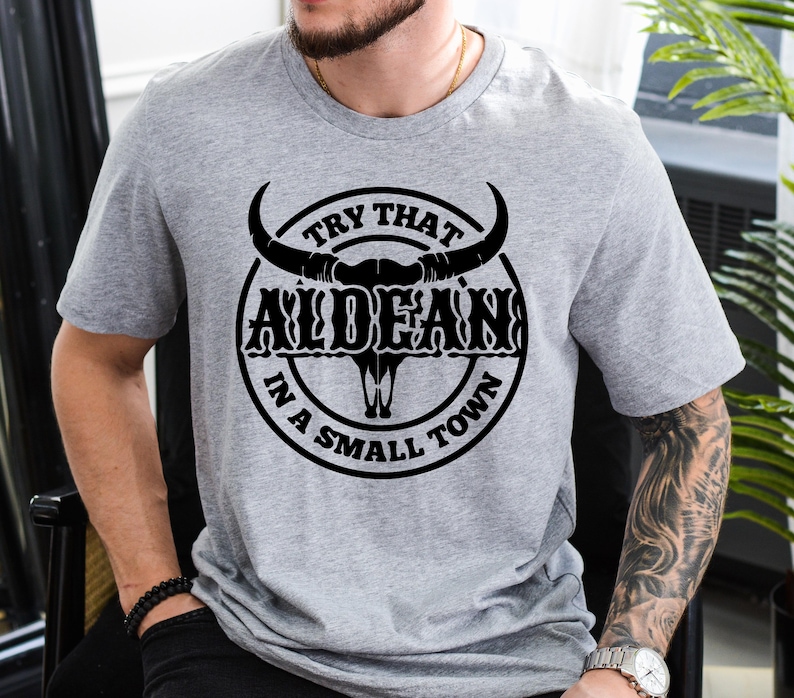 May include: Gray t-shirt with a black bull skull graphic and the text "Try That In A Small Town" and "ALDEAN".