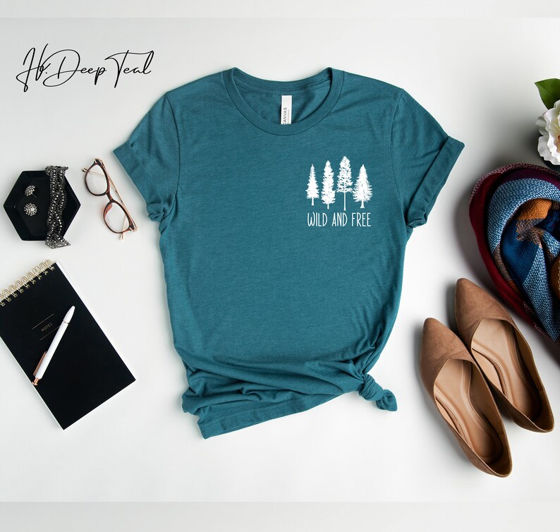 May include: Teal blue t-shirt with a white graphic of five trees and the text "Wild and Free".