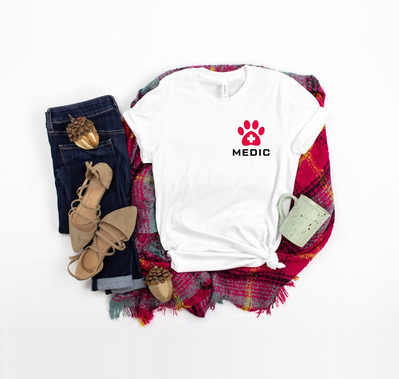 May include: White t-shirt with a red paw print with a white plus sign in the center and the word "MEDIC" in black letters below the paw print.