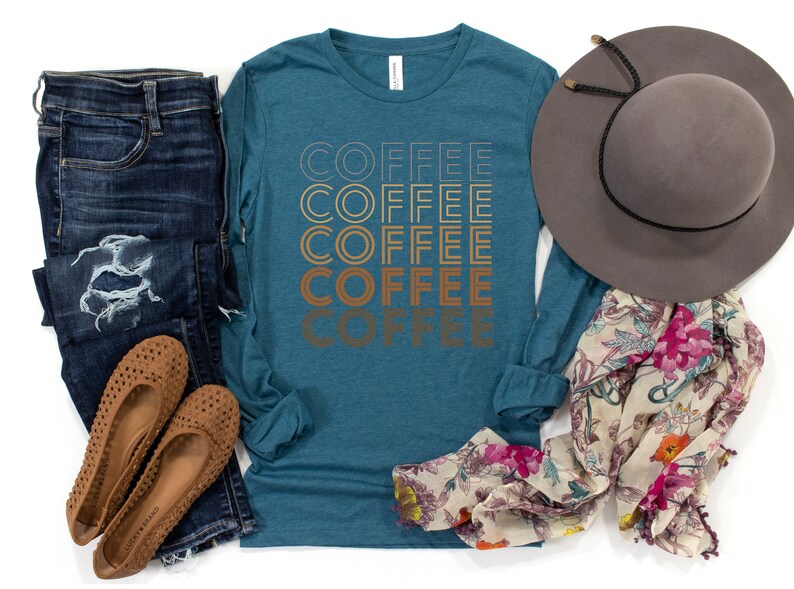K&ouml;nnte beinhalten: Ein blaues Langarmshirt mit dem Wort "COFFEE", das f&uuml;nfmal in einer Retro-Schrift wiederholt wird. Das Shirt wird mit einer blauen Jeans, braunen Ballerinas, einem floralen Schal und einem braunen Fedora kombiniert.