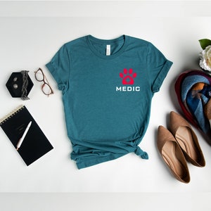 May include: Teal blue t-shirt with a red paw print and the word "MEDIC" in white lettering.