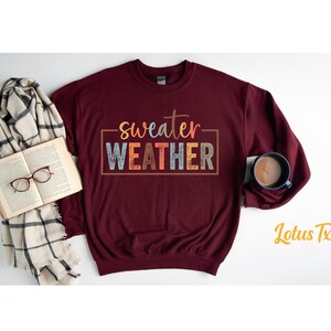 May include: A maroon sweatshirt with the text "sweater weather" in colorful letters. The text is in a box with a white outline.
