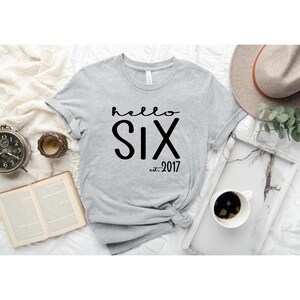 May include: Gray t-shirt with the text "hello six est. 2017" printed in black.