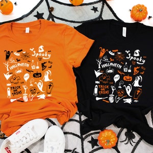 Puede incluir: Dos camisetas con tem&aacute;tica de Halloween. Una es naranja con gr&aacute;ficos negros y la otra es negra con gr&aacute;ficos naranjas. Ambas camisetas presentan una variedad de iconos de Halloween, incluyendo fantasmas, calabazas, murci&eacute;lagos y un sombrero de bruja. El texto en las camisetas dice "Spooky Halloween" y "Trick or Treat".