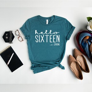 May include: Teal blue t-shirt with white text that reads "hello sixteen est. 2006".