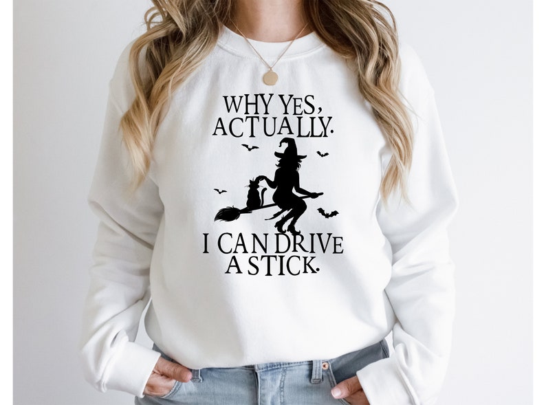May include: White sweatshirt with a black graphic of a witch flying on a broomstick with a cat. The text reads "Why yes, actually. I can drive a stick."