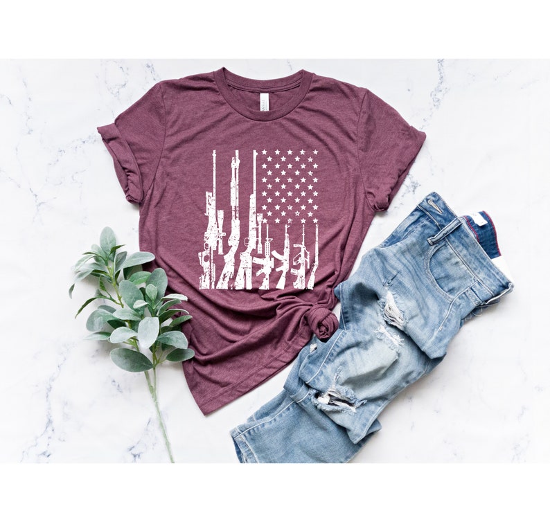 May include: A maroon t-shirt with a white graphic of an American flag made up of guns.