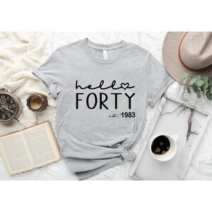 May include: Gray t-shirt with black text that reads "hello forty est. 1983" with a small heart symbol.