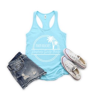 May include: A light blue tank top with a white graphic of palm trees and the text "Miami Beaches Nasha's Dirty Thirty".