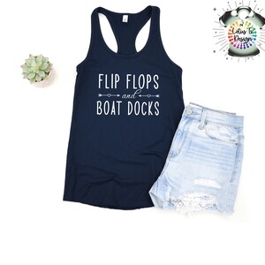 May include: A navy blue tank top with the text "Flip Flops and Boat Docks" in white lettering. The text is centered on the shirt and is surrounded by two arrows pointing in opposite directions.