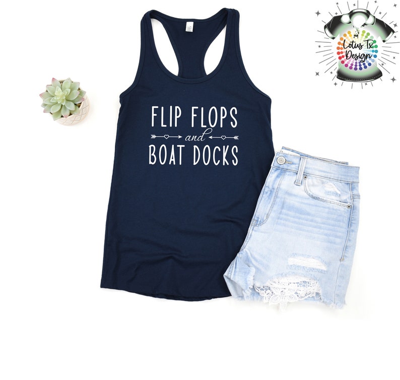 May include: A navy blue tank top with the text "Flip Flops and Boat Docks" in white lettering. The text is centered on the shirt and is surrounded by two arrows pointing in opposite directions.