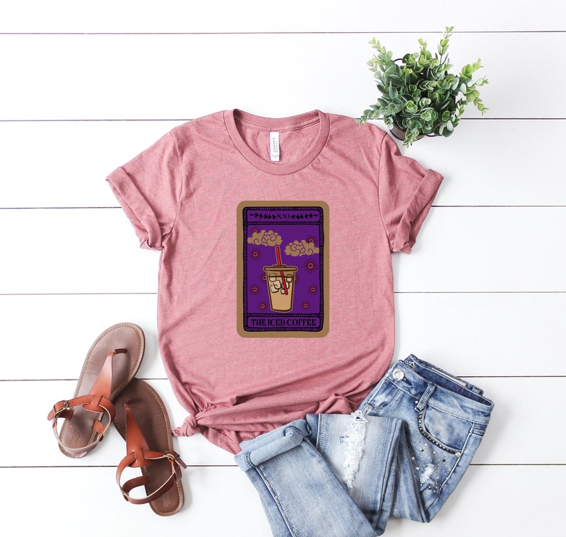 Puede incluir: Una camiseta rosa con un gr&aacute;fico de una carta de tarot que presenta una taza de caf&eacute; helado con el texto "The Iced Coffee".