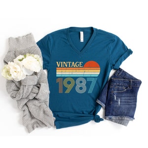 Peut inclure: T-shirt bleu sarcelle &agrave; col en V avec un graphique de coucher de soleil vintage et le texte "Vintage 1987".